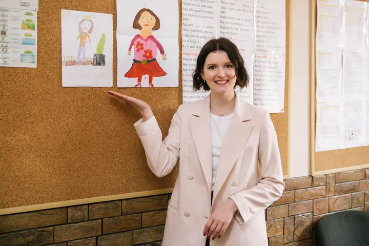 A teacher shows children's drawings on the classroom wall