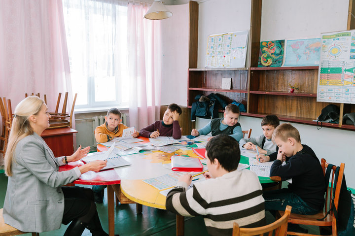 A teacher and a group of children work with teaching materials at a shared table